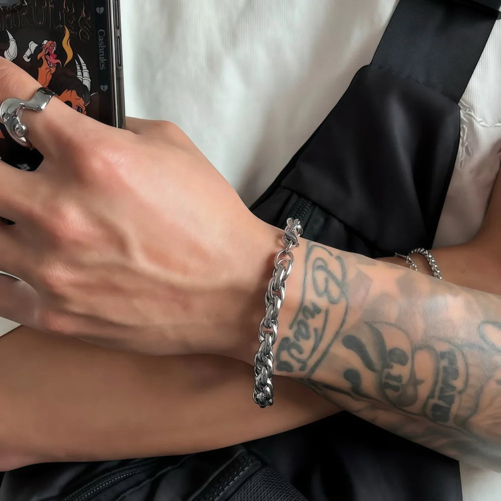 Close-up of a person's arm with a silver chain bracelet and tattoo, holding a phone.